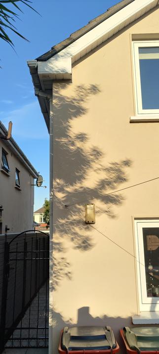 Strange crescent shapes from leaves of a tree projected onto a wall of a house, caused by the eclipse at its maximum.