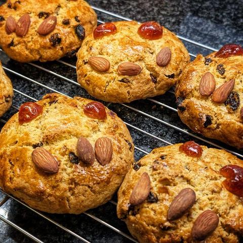 A photo of some golden baked cake type things, with glace cherries for eyes and almonds for teeth, as is customary for Fat Rascals. They're cooling on a rack.