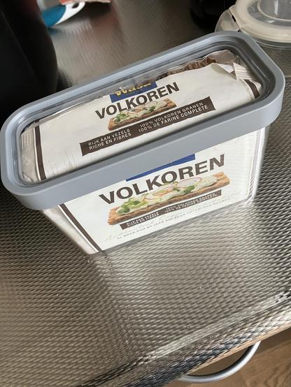 Papieren pak volkoren crackers in een doorzichtige plastic doos met grijze rand door het deksel waar het precies in past