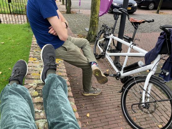 Stenen muurtje met daarop twee benen en een op het hoofd na volledig mens. Ernaast staat een ebike.