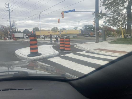 We are at a light. A concrete corner has been placed on the other side of a crosswalk, with space between it and the street corner, accommodating the bike lane to our right.